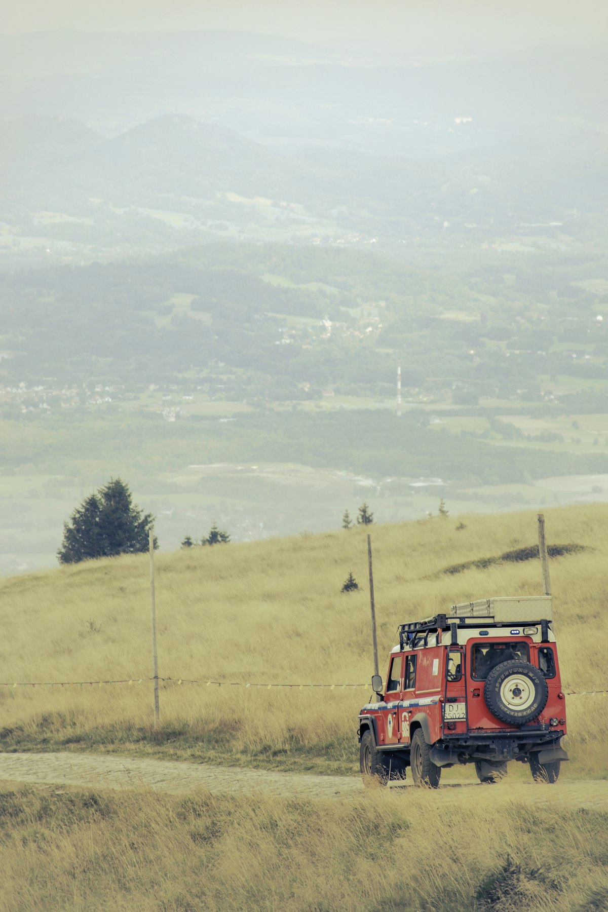 Red off-road SUV parked on a grassy hilltop overlooking a valley