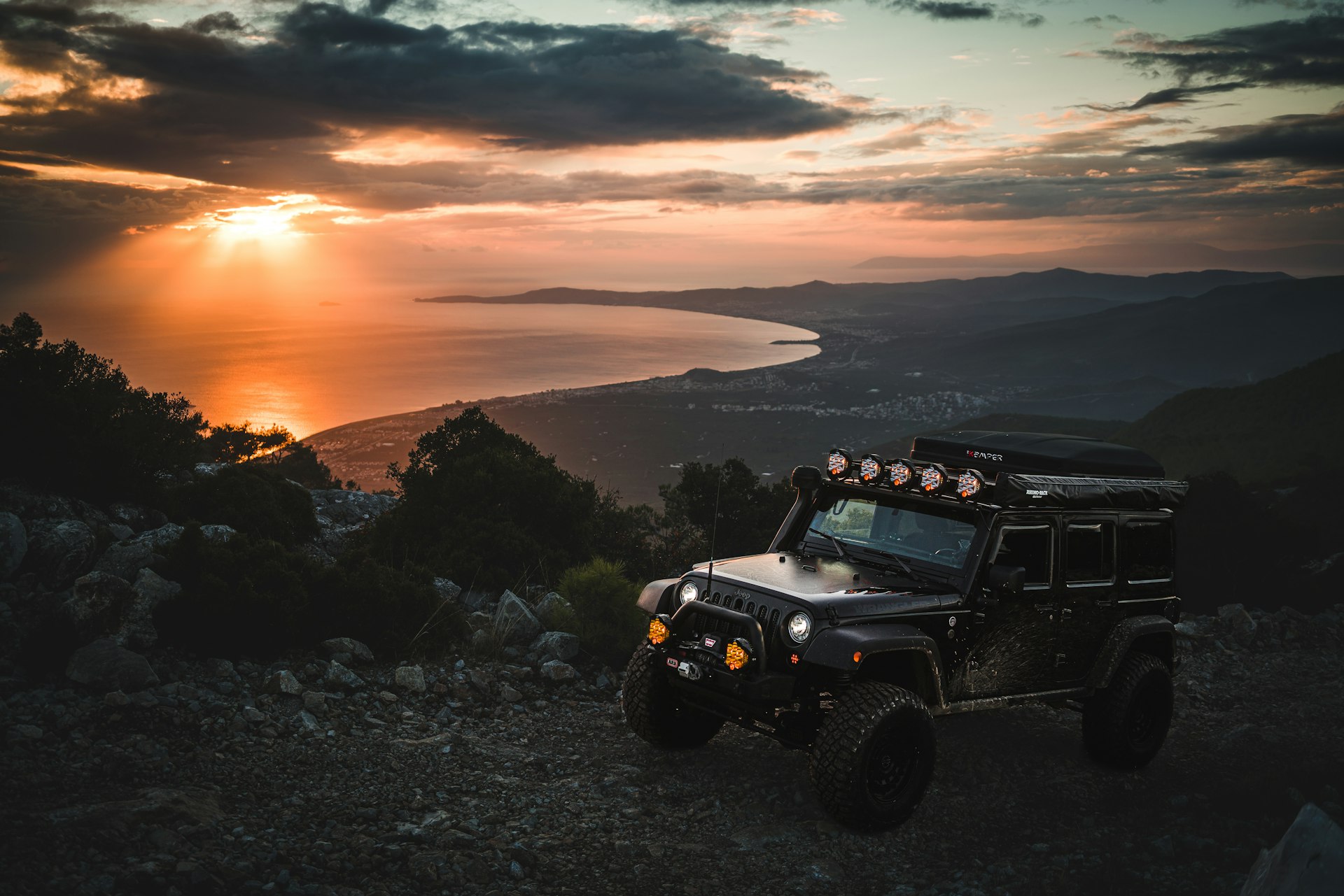 Off-road jeep parked on a mountain ridge above the coast at golden hour