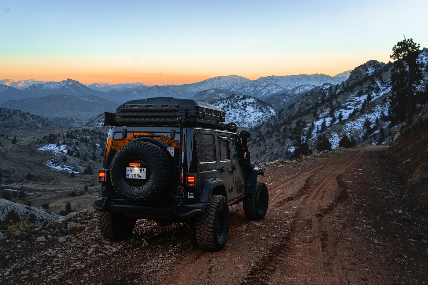 Off-road jeep parked on a rocky mountain trail with a sunset skyline