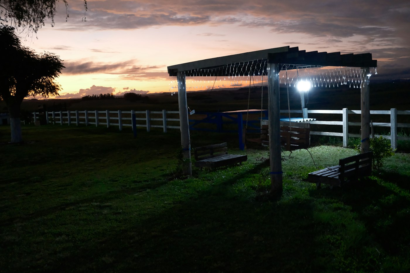 Rural farmhouse pergola and swing bench at dusk, evening light