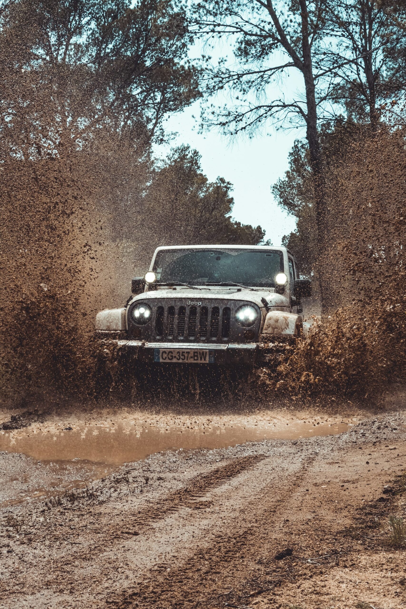 Jeep driving through a muddy off-road trail, water and mud splashing